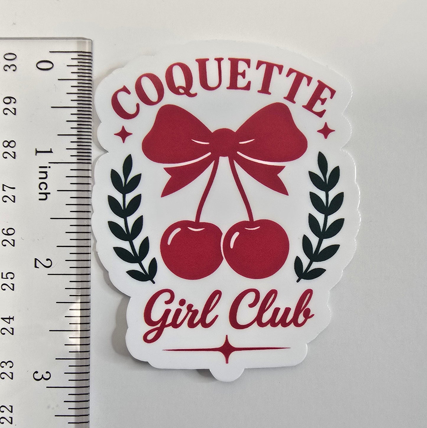 Coquette Girl Club sticker with red bow and cherries, surrounded by black laurel leaves on a white die-cut background.