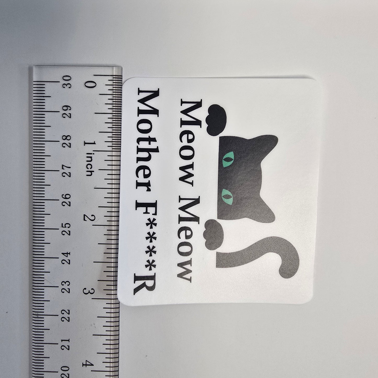 Sticker with a cat graphic and text next to a ruler for size reference on a gray background