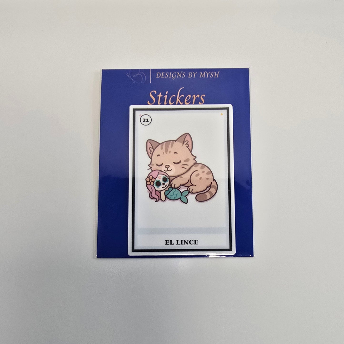 Vinyl sticker depicting a cute lynx cat with yarn and sugar skull in a Lotería card style labeled “El Lince.”