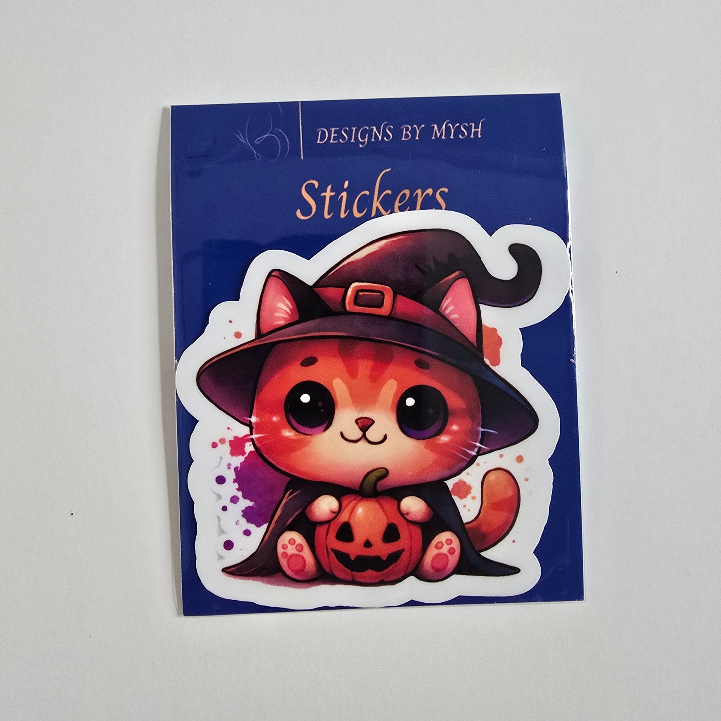 Cute vinyl sticker of an orange tabby cat in a witch hat holding a jack-o'-lantern pumpkin, Halloween-themed on a blue branded backing card.