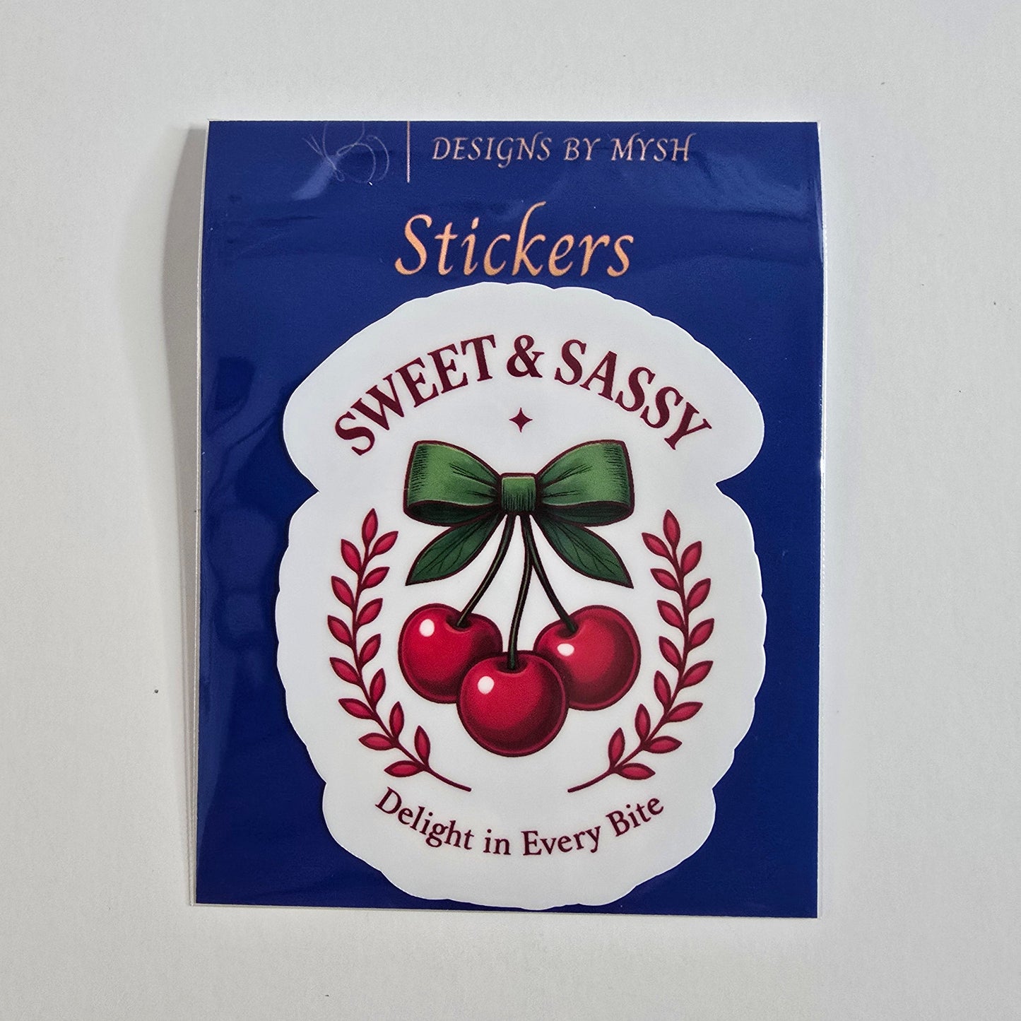 Retro-style cherry sticker with three red cherries tied in a green bow and labeled “Sweet & Sassy” with “Delight in Every Bite.”