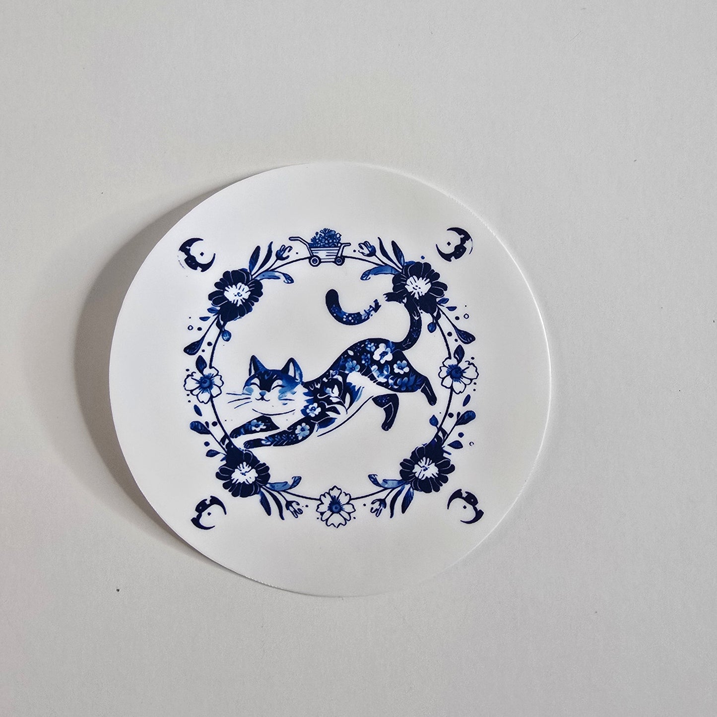 Round white coaster with blue floral and deer design on a light gray background