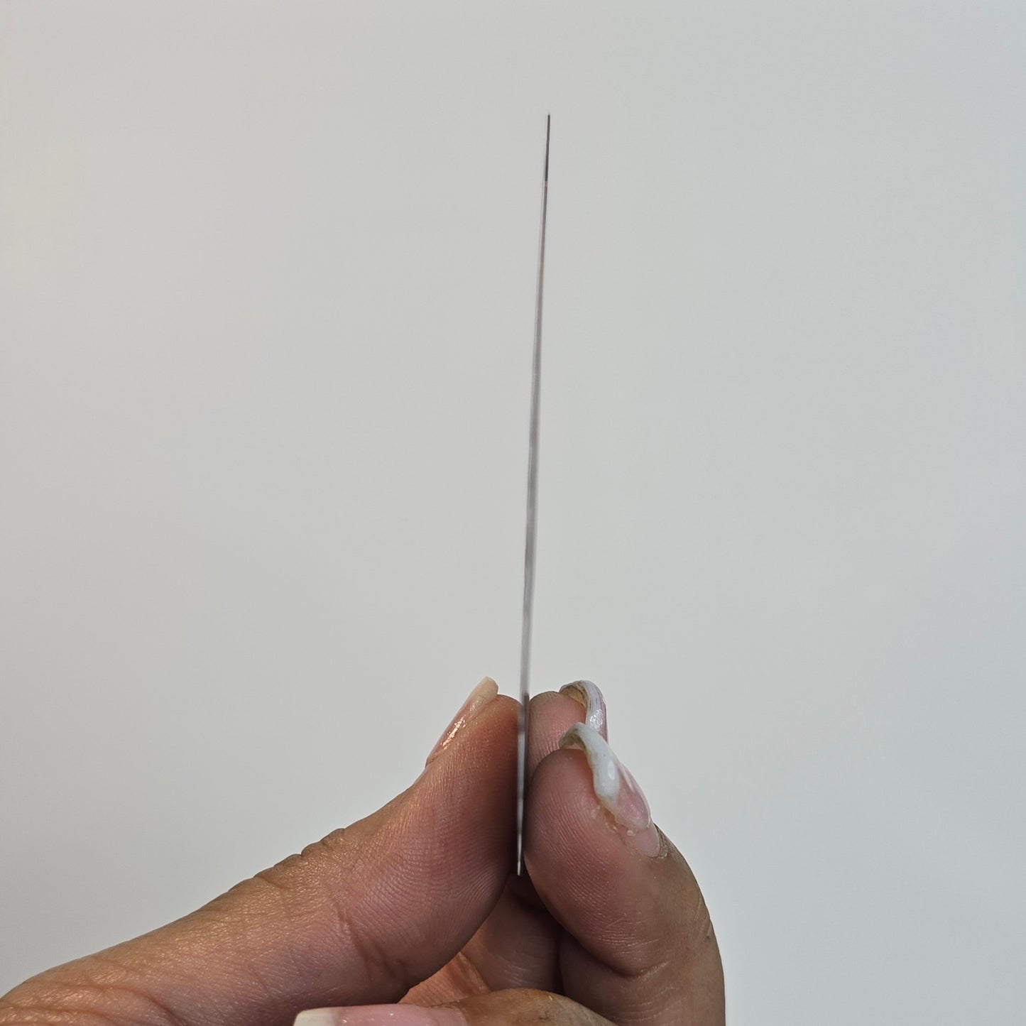 Hand holding a thin metal rod against a plain background