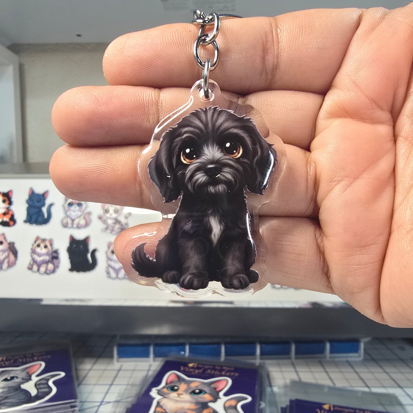 Black dog-shaped keychain held in a hand with a display of similar keychains in the background.
