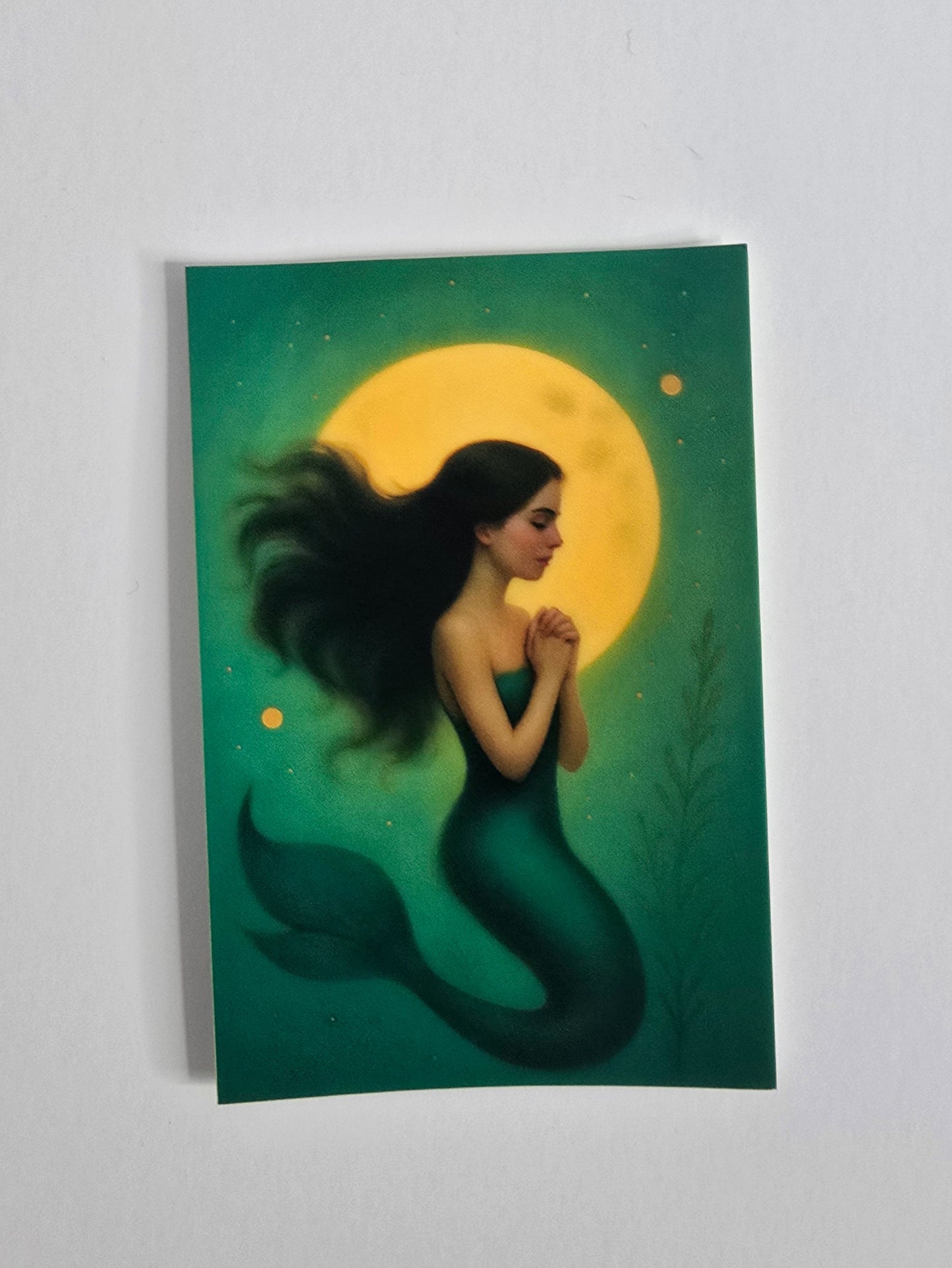 "Illustrated mermaid sticker featuring a mystical woman with flowing black hair in front of a glowing yellow moon, printed on a 3-inch die-cut laminated vinyl sticker."