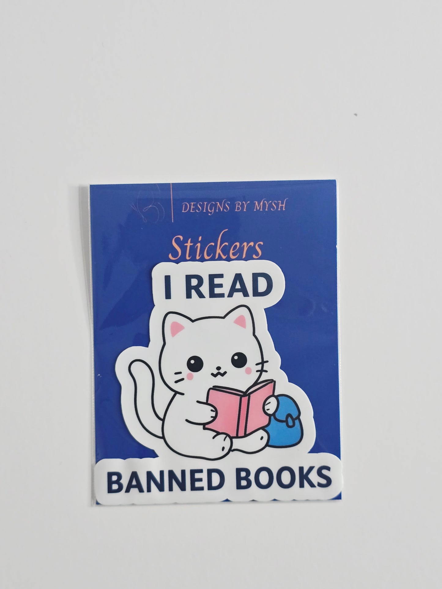 "Vinyl sticker featuring a white cartoon cat reading a pink book with the phrase 'I Read Banned Books' in bold text, 3-inch waterproof die-cut sticker."