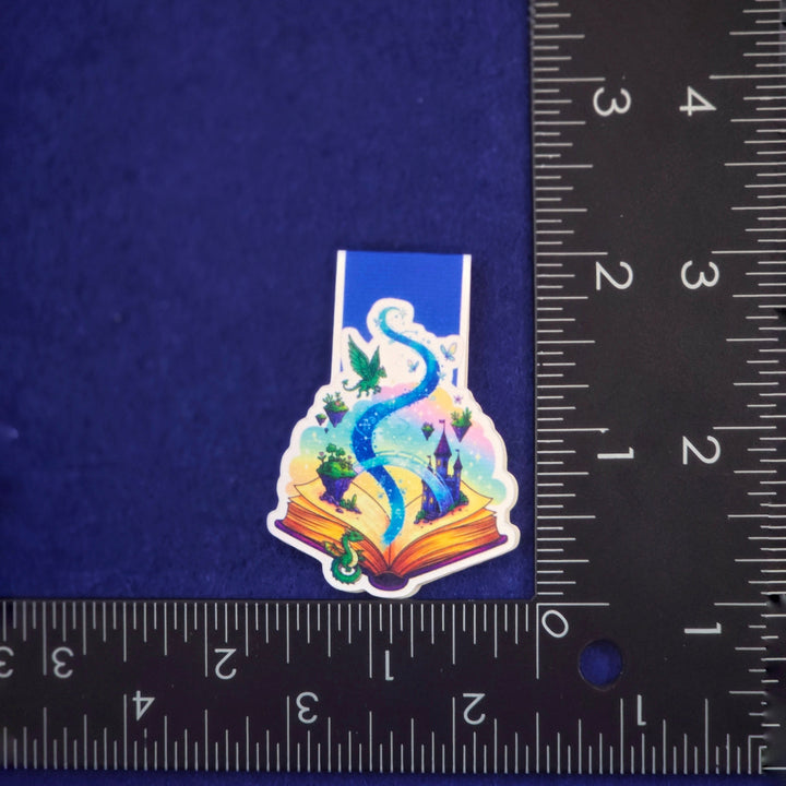 Colorful sticker of a dragon on an open book with a ruler for scale on a blue background