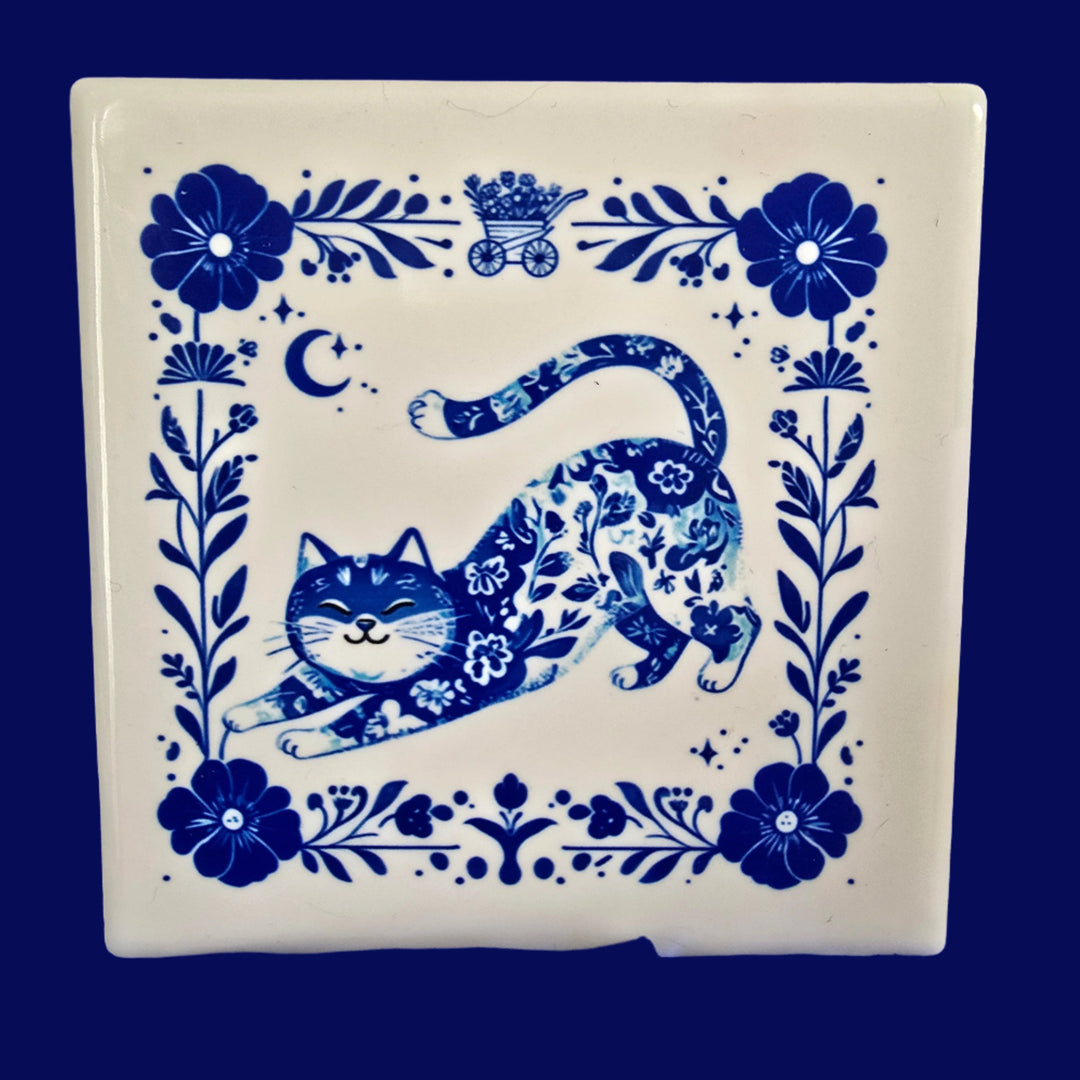 A square ceramic coaster with a whimsical blue cat design surrounded by floral patterns against a white background.