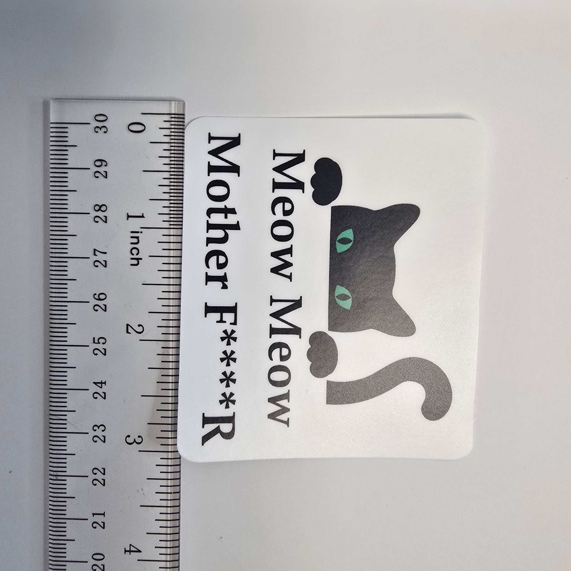 Sticker with a cat graphic and text next to a ruler for size reference on a gray background