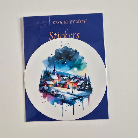 Round vinyl sticker of a watercolor winter village at night with glowing houses, pine trees, and a blue moonlit sky.