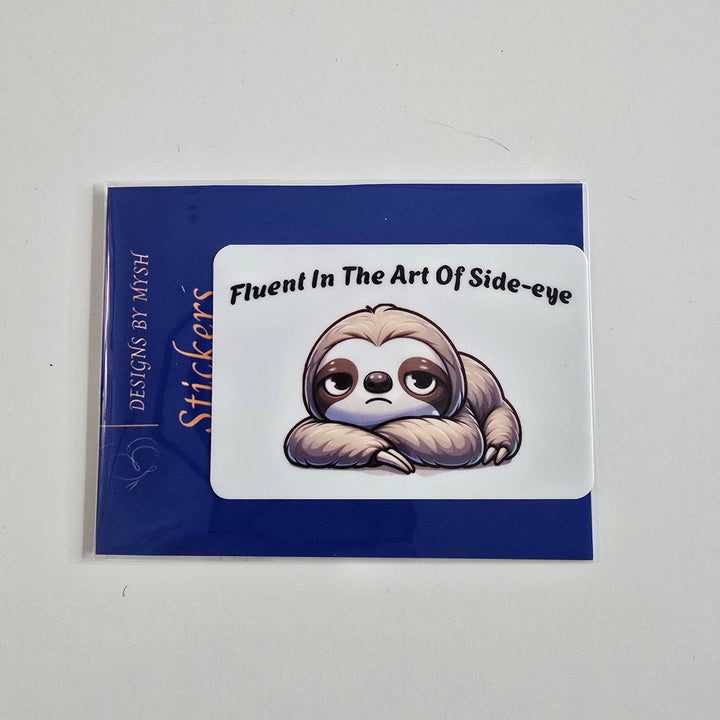Funny vinyl sticker of a grumpy cartoon sloth with arms crossed and the text “Fluent In The Art Of Side-eye”.