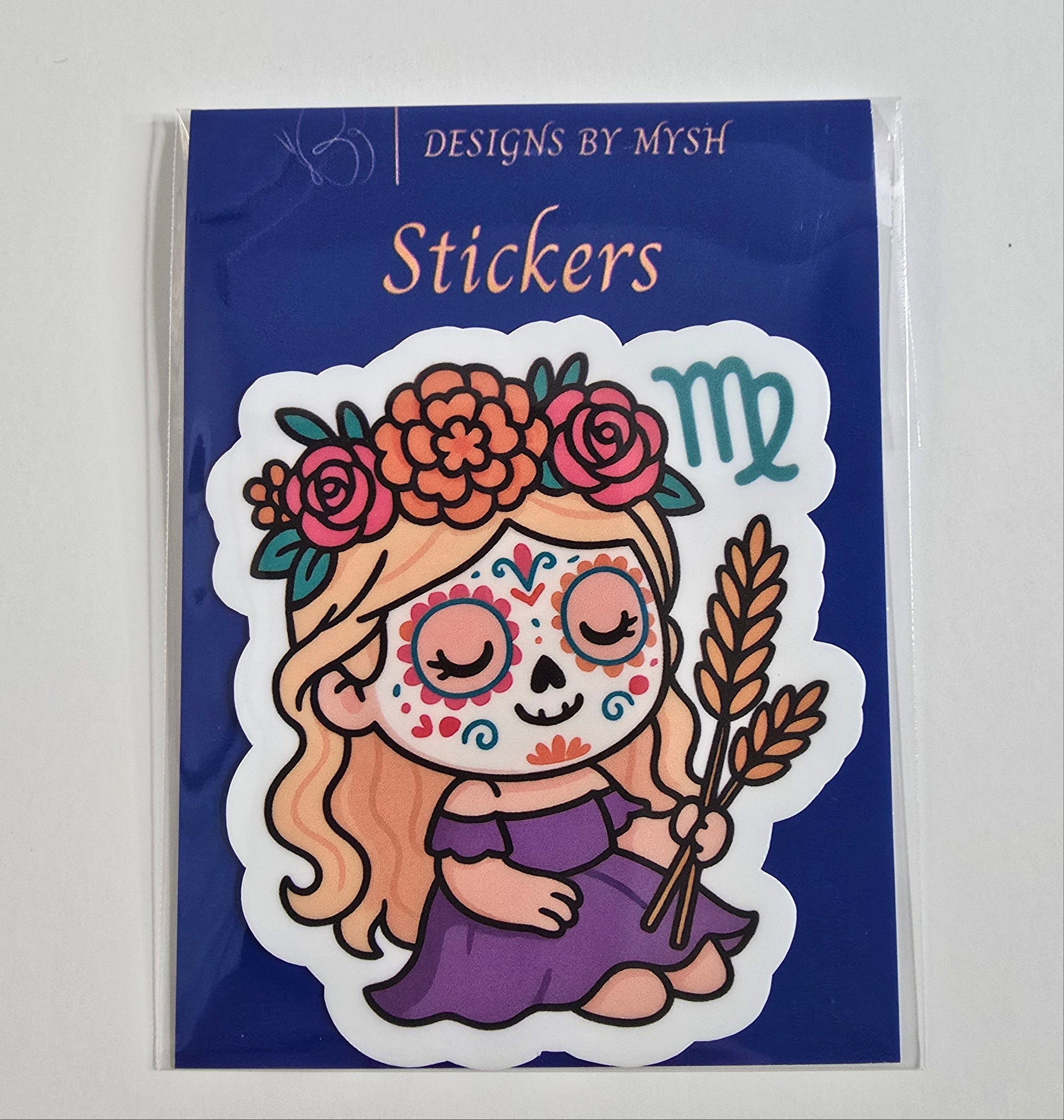 Vinyl sticker of a sugar skull girl in a purple dress holding a wheat stalk with Virgo zodiac symbol and floral crown, on branded backing card.
