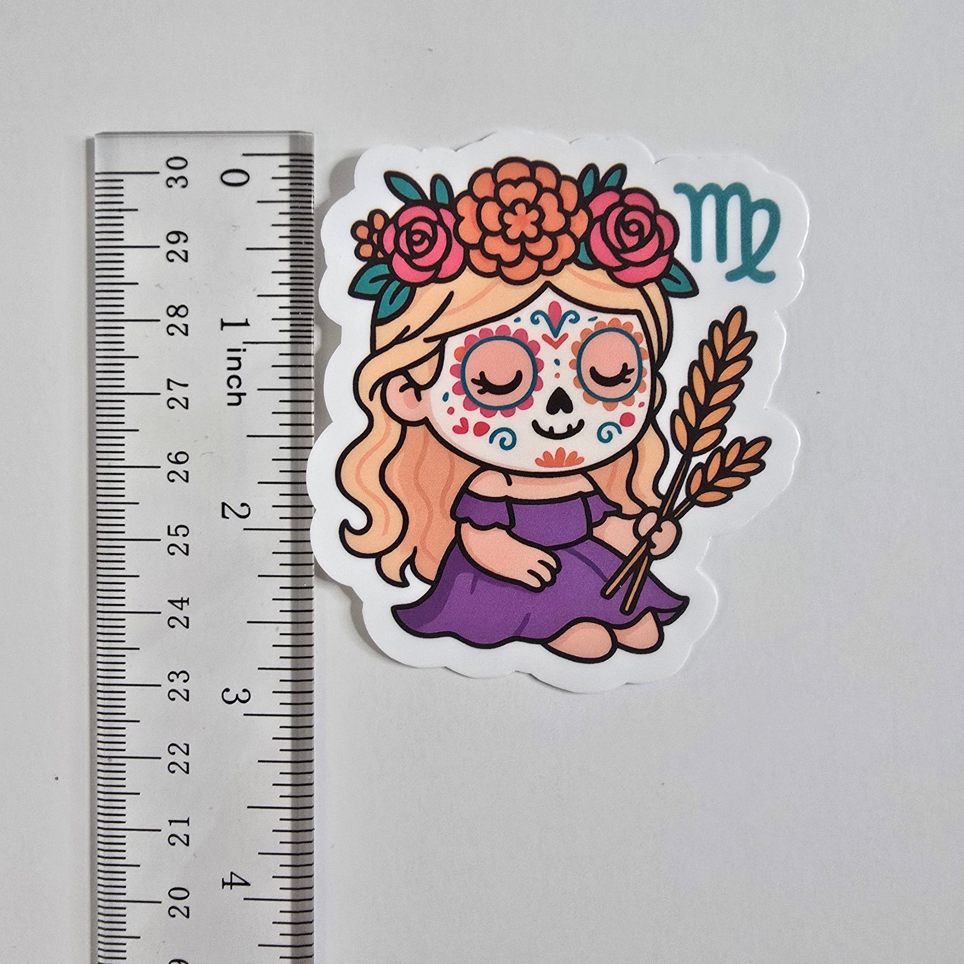 Sticker of a colorful design with a face and flowers next to a ruler for scale on a gray background