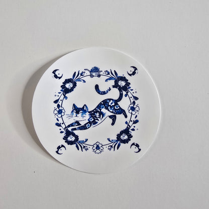 Round white coaster with blue floral and deer design on a light gray background
