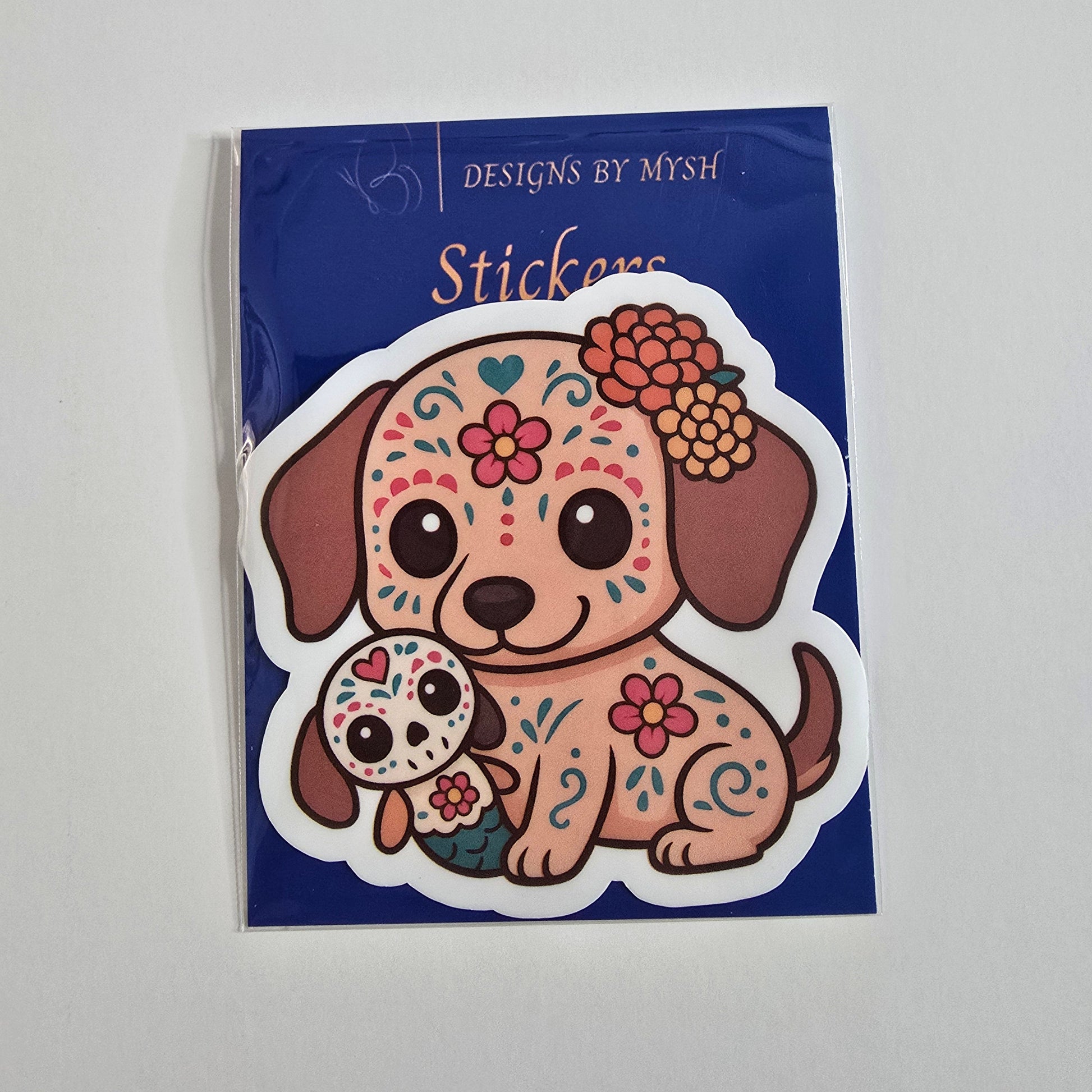 Sticker of a cute dog with sugar skull designs, floral headpiece, and a mini calavera doll, themed for Día de los Muertos.