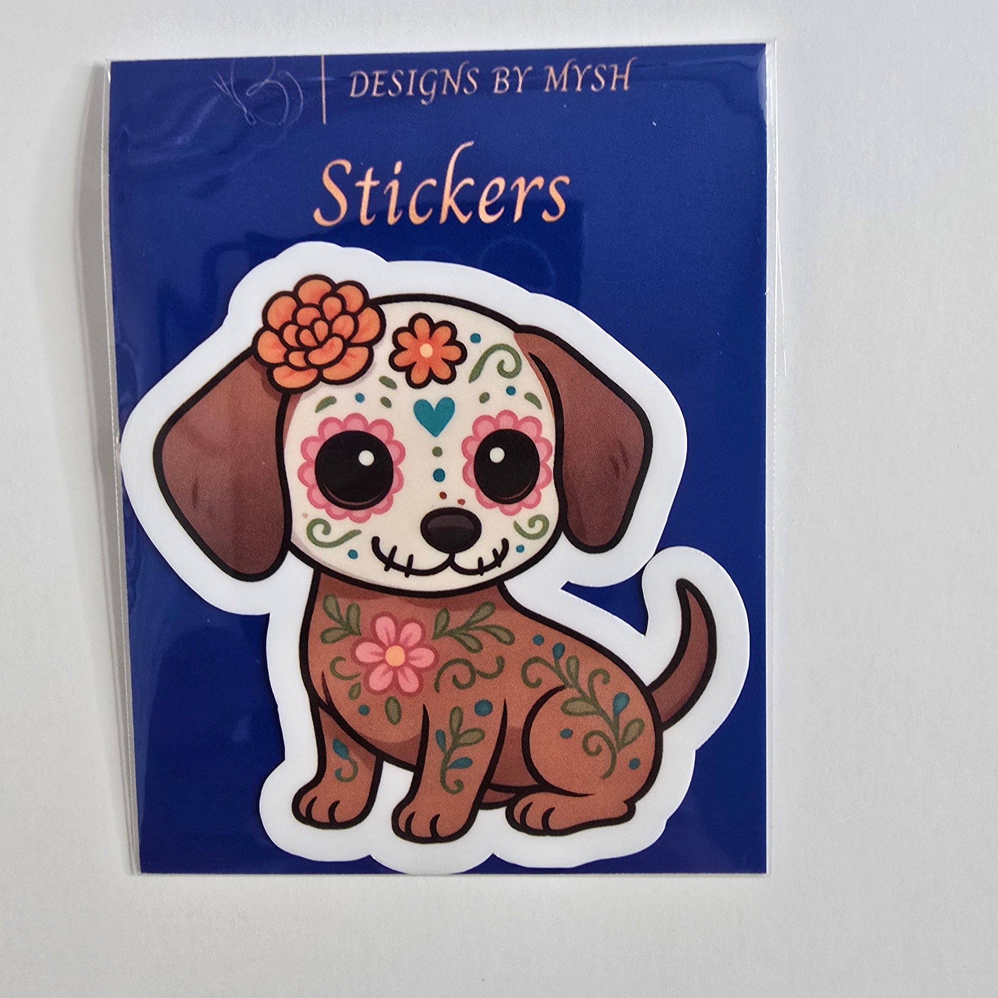 Vinyl sticker of a brown cartoon dog with sugar skull and floral Día de los Muertos designs.
