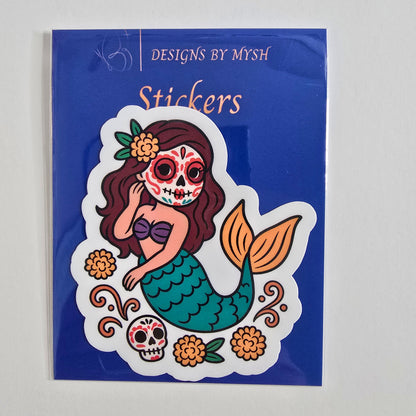 Vinyl sticker of a mermaid with a sugar skull face, colorful flowers, and Día de los Muertos-themed decorations.
