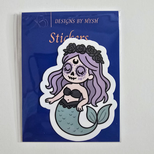 Sticker of a pastel goth mermaid with lavender hair, sugar skull makeup, flower crown, and seafoam tail on a white background.