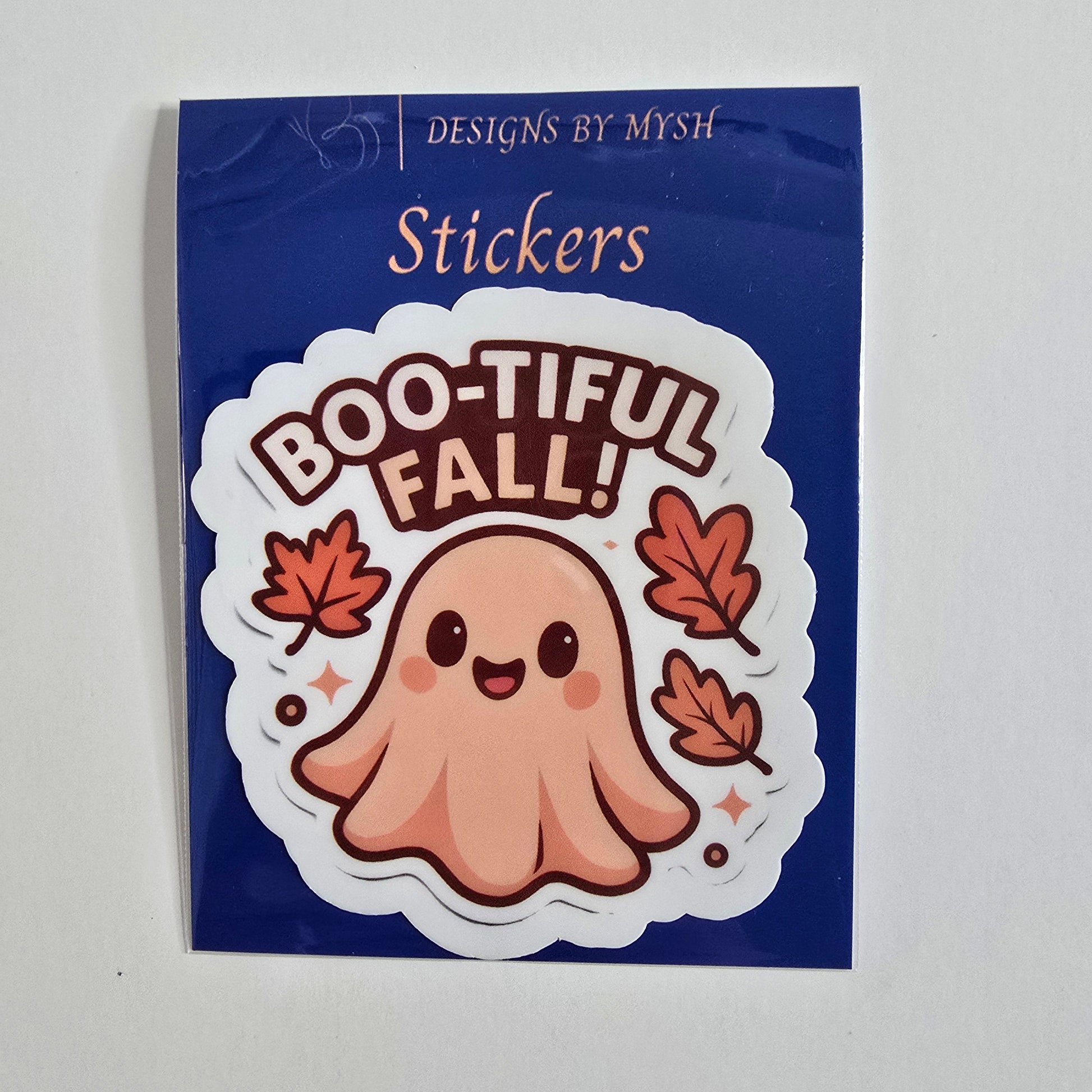 Vinyl die-cut sticker of a cute peach-toned ghost with a smiling face surrounded by falling orange autumn leaves and the phrase “Boo-tiful Fall!”