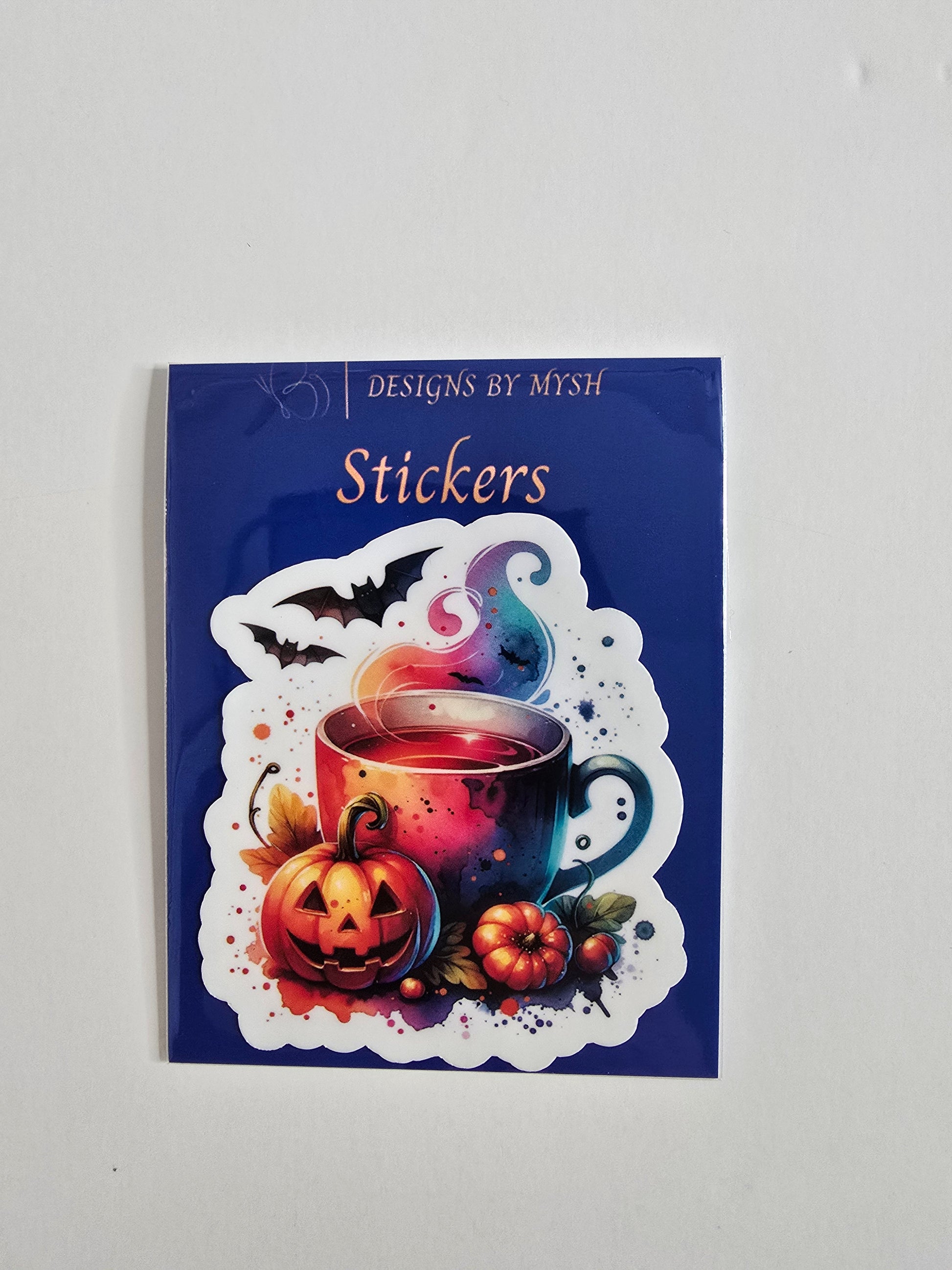 Halloween-themed vinyl sticker with a steaming mug, pumpkins, bats, and colorful spooky design in vibrant tones on a die-cut shape.