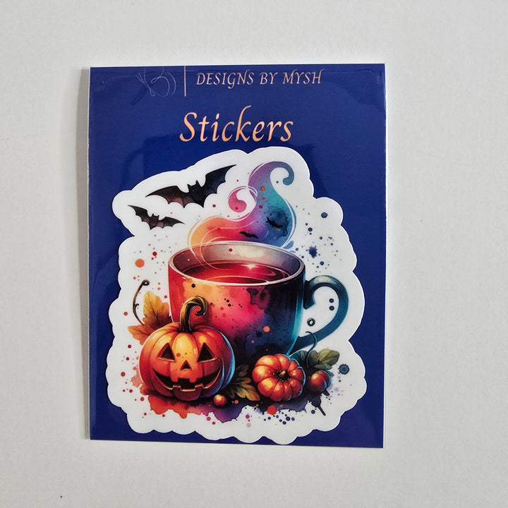 Halloween-themed vinyl sticker with a steaming mug, pumpkins, bats, and colorful spooky design in vibrant tones on a die-cut shape.