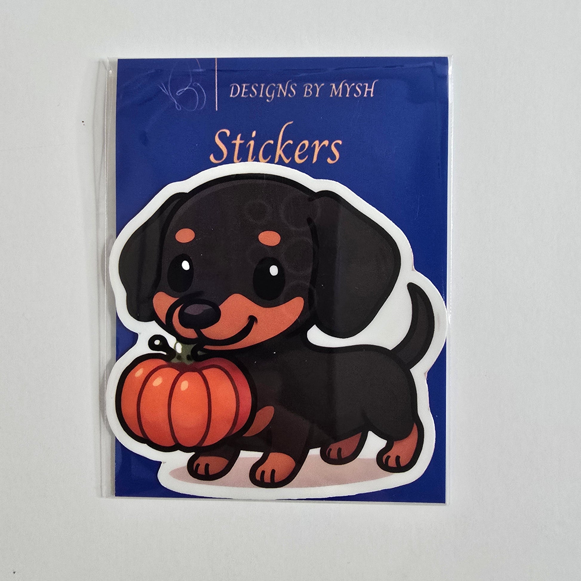 Sticker of a black and tan dachshund holding an orange pumpkin in its mouth on a white background.
