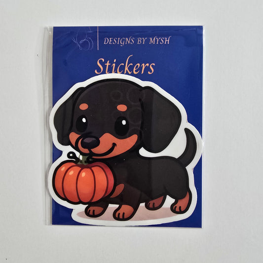 Sticker of a black and tan dachshund holding an orange pumpkin in its mouth on a white background.