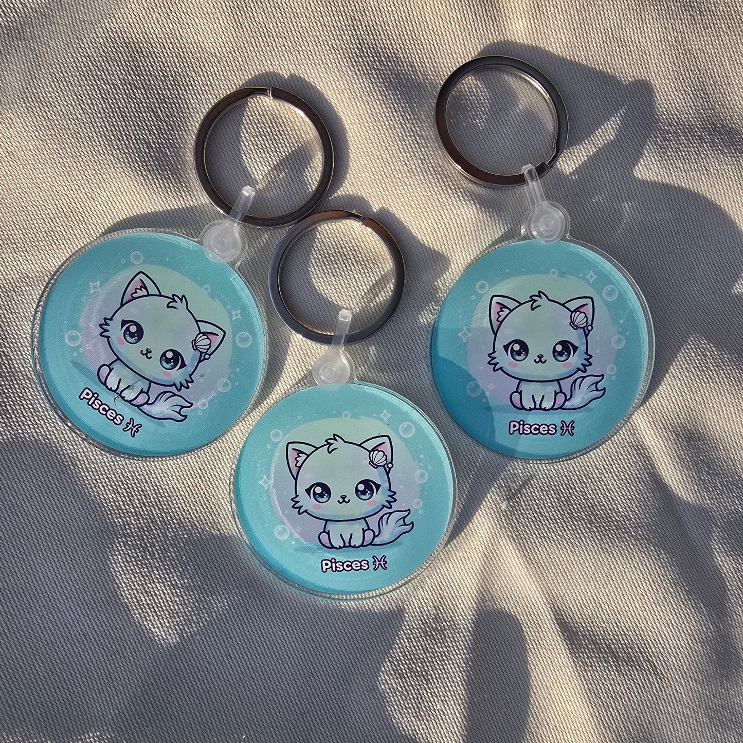 Three kawaii Pisces keychains arranged on fabric with shadows, astrology-themed accessories