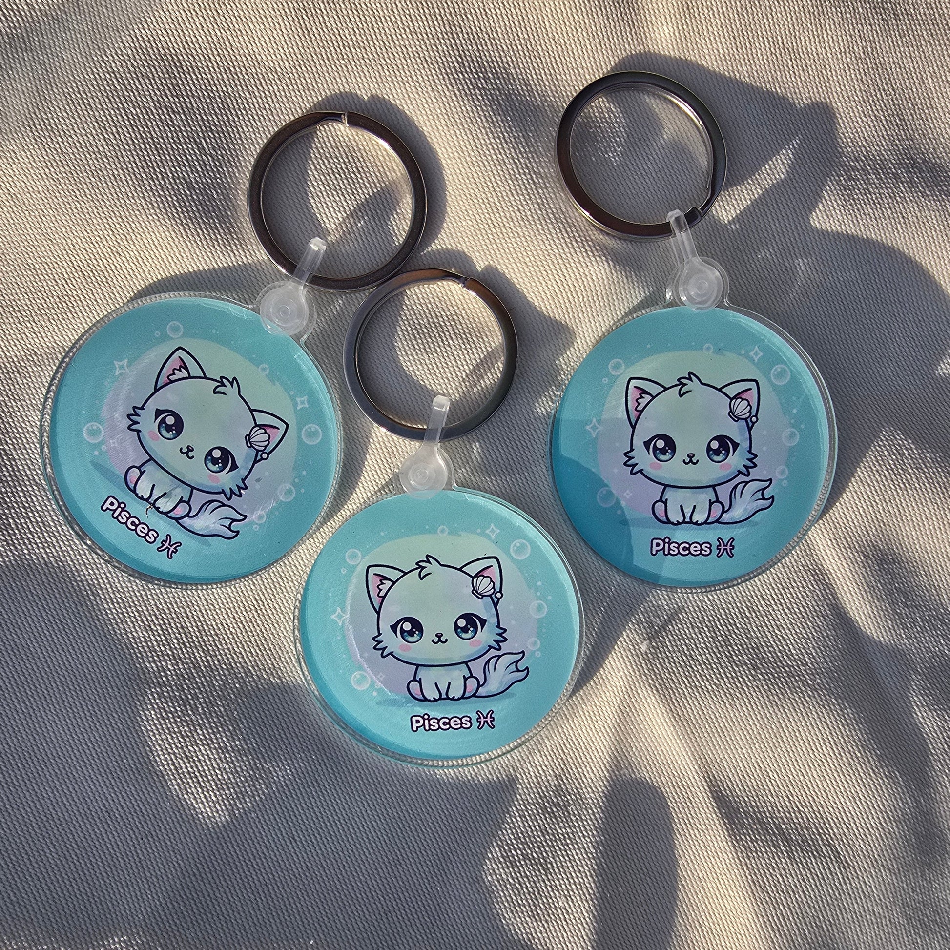 Three kawaii Pisces keychains arranged on fabric with shadows, astrology-themed accessories