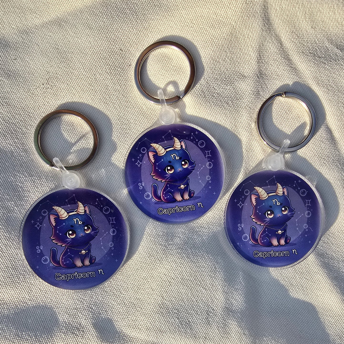 Three blue keychains with cat designs on a textured surface