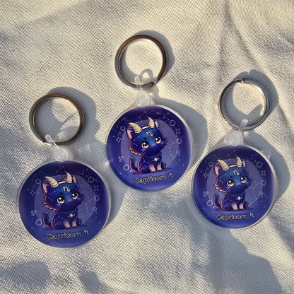 Three blue keychains with cat designs on a textured surface