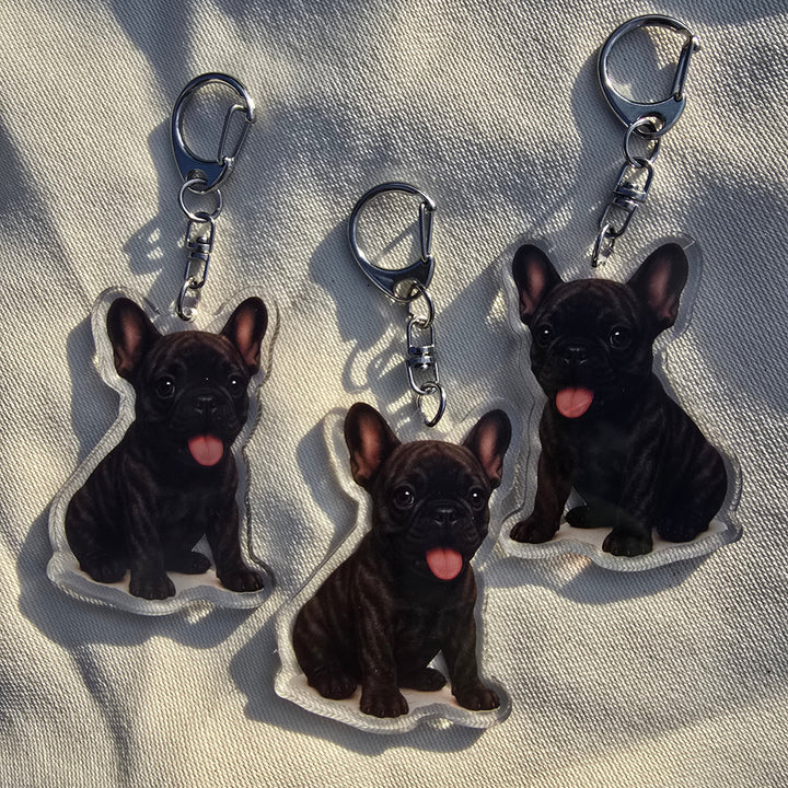 Three black dog-shaped keychains on a beige fabric background