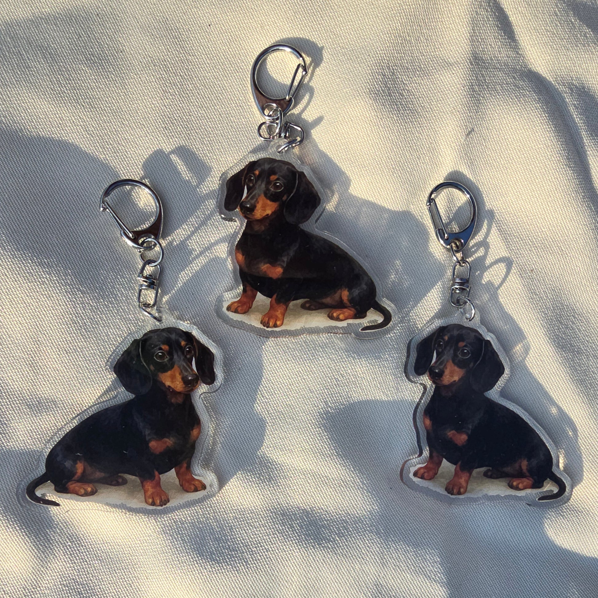 Three Dachshund-shaped keychains on a light fabric background