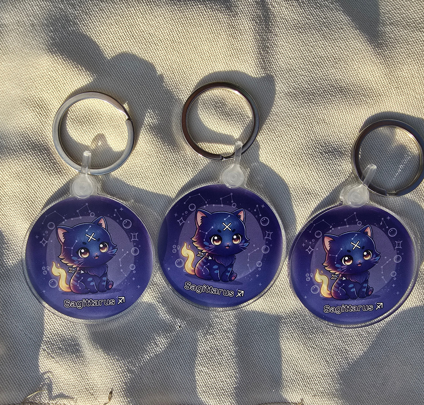 Three blue cat-shaped keychains on a textured fabric background