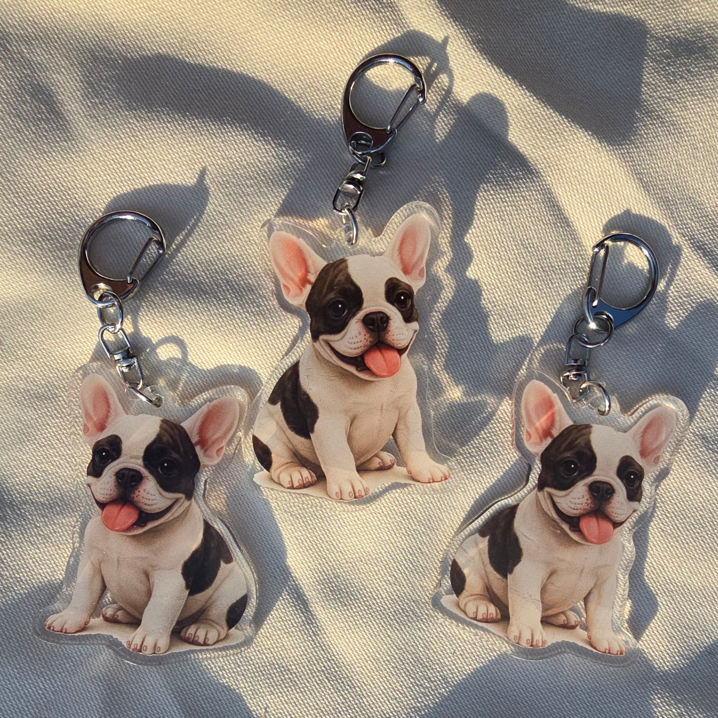 Three white and black French Bulldog acrylic keychains with tongue out and lobster clasps on canvas fabric