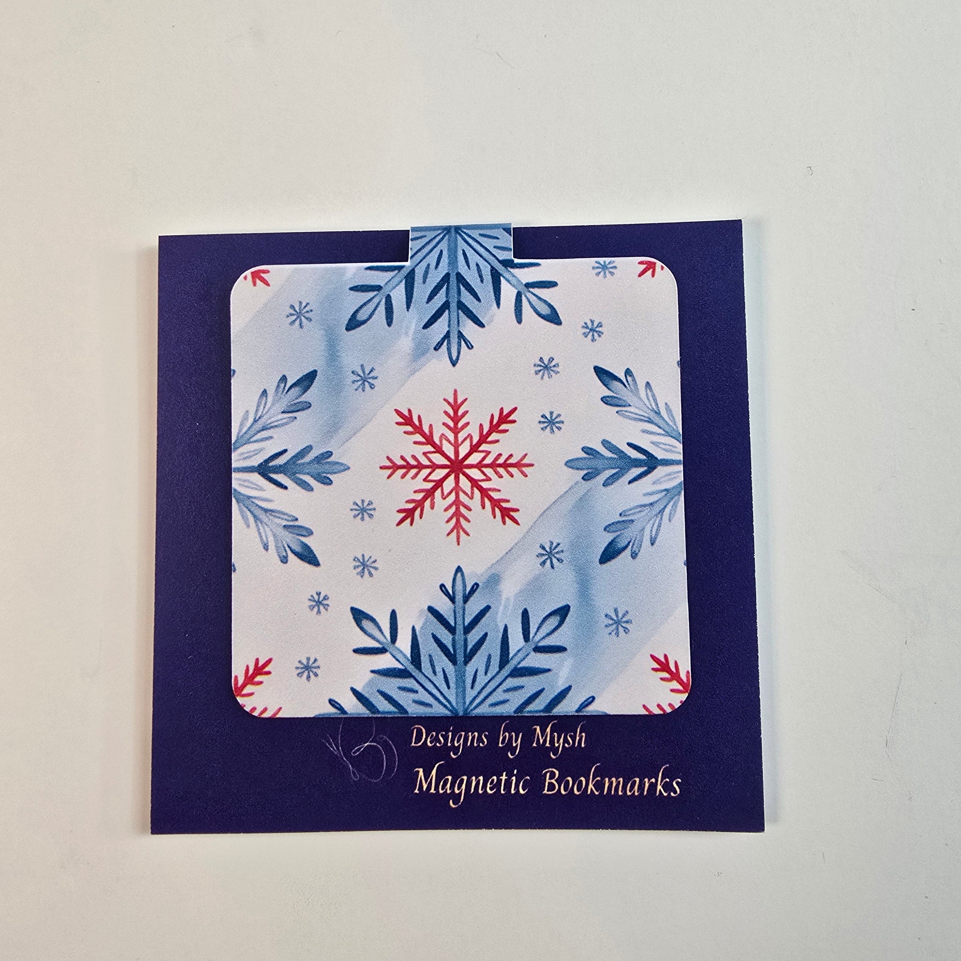 Magnetic bookmark featuring blue and red snowflakes on a soft winter-themed background – by Designs by Mysh.