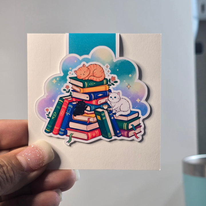 Colorful magnetic bookmark of books and cats held by a hand on a light background