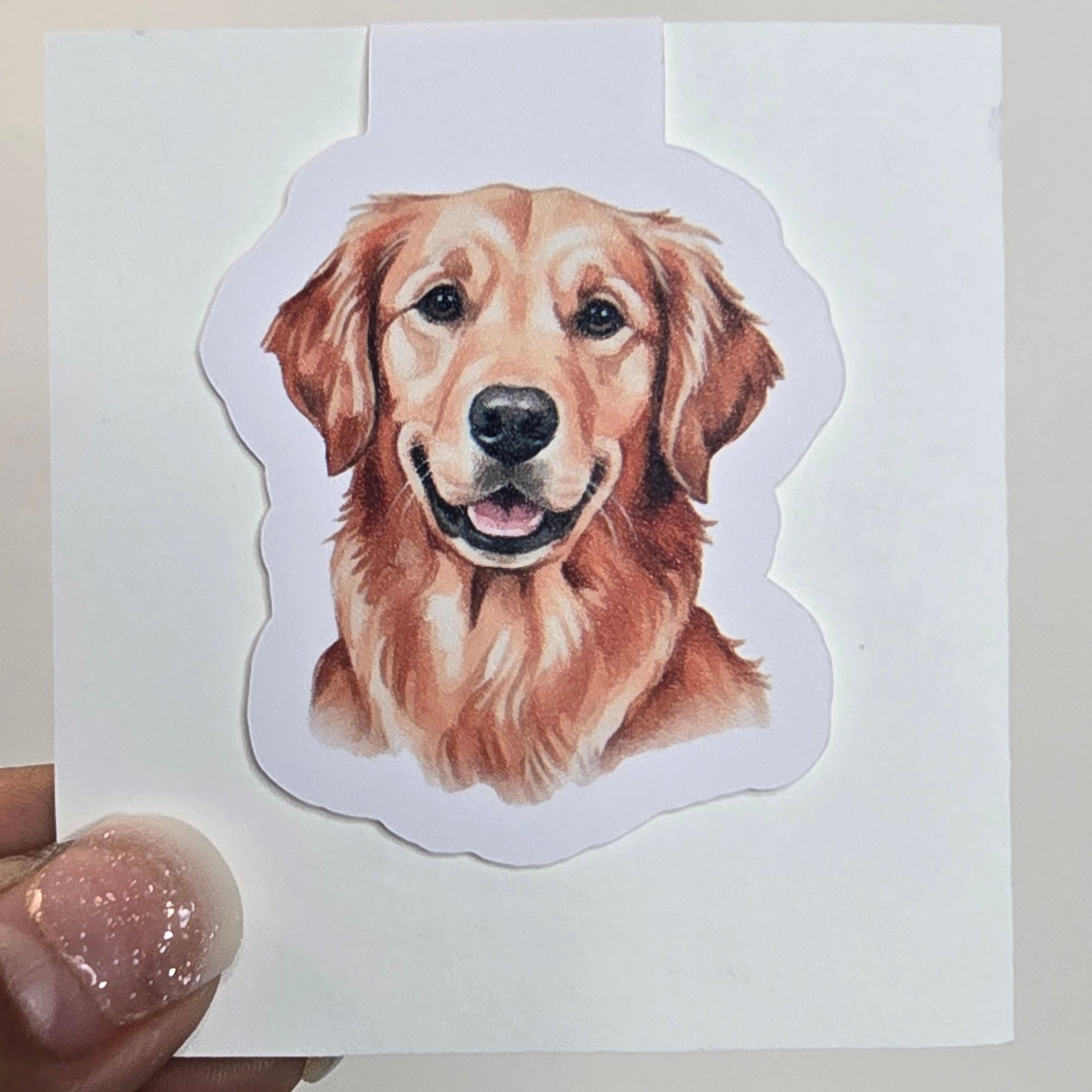 Sticker of a golden retriever held over a white card with a grid pattern.