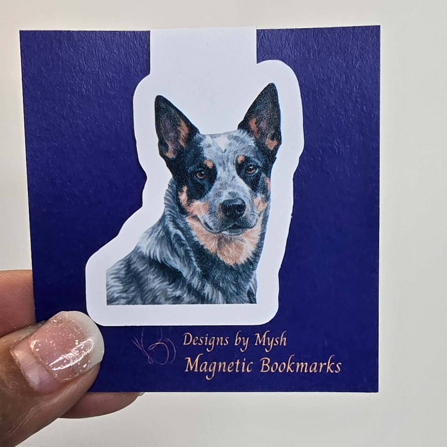 Magnetic bookmark with a dog design on a blue card held by a hand.