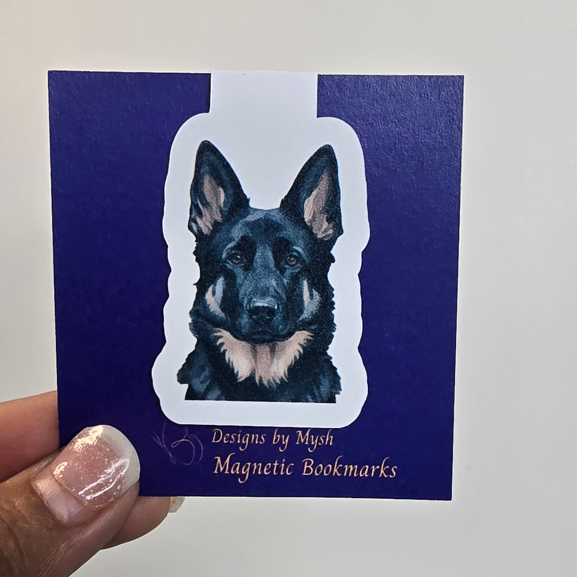 Hand holding a blue bookmark with a dog illustration and text on a white background
