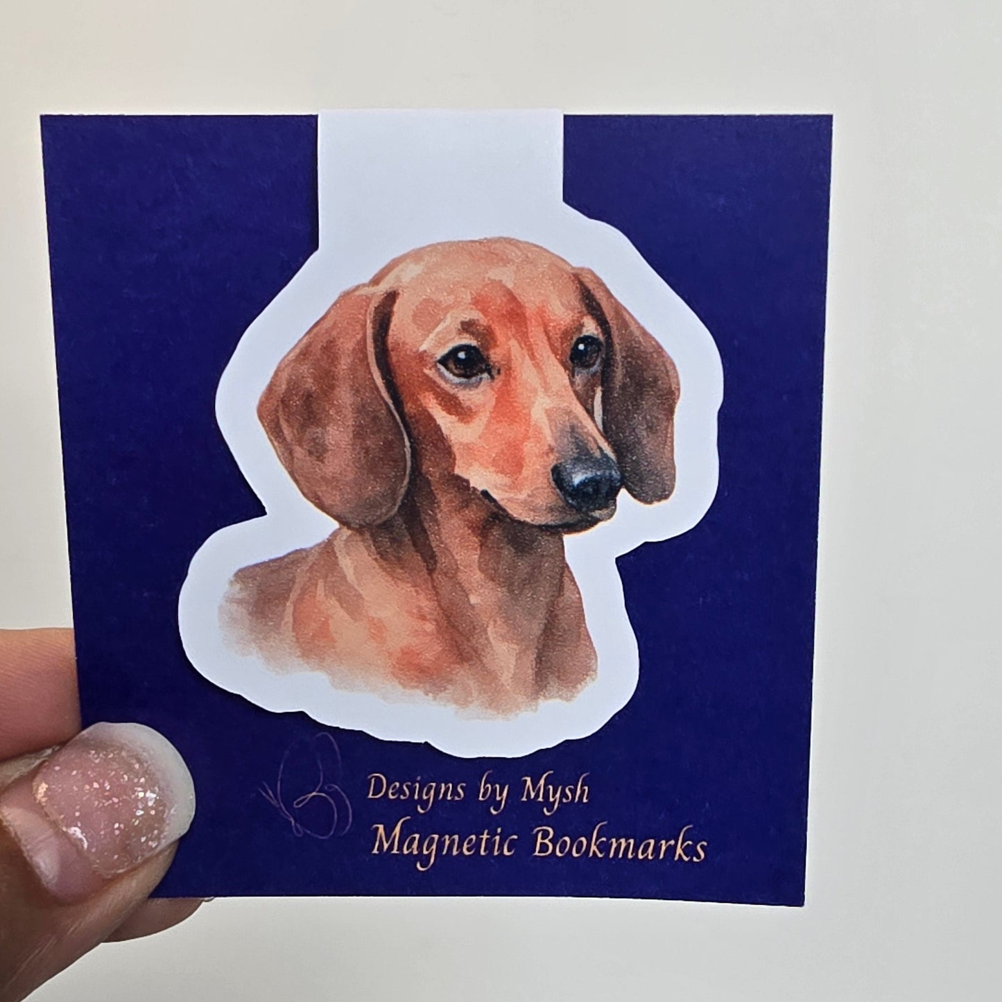 Magnetic bookmark with a dog design on a blue card held by a hand.