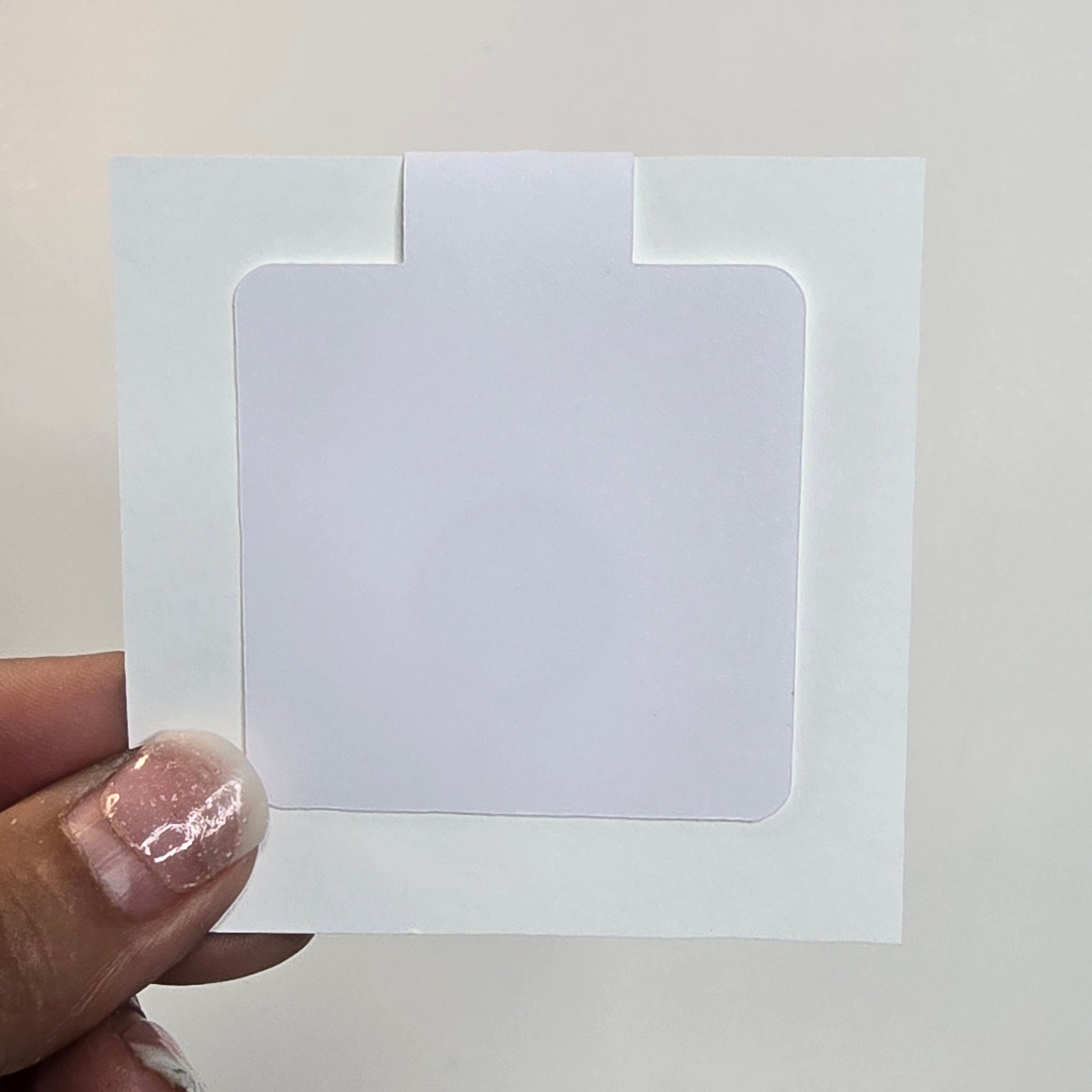 White card with a cut-out square held by a hand against a grid-patterned wall.