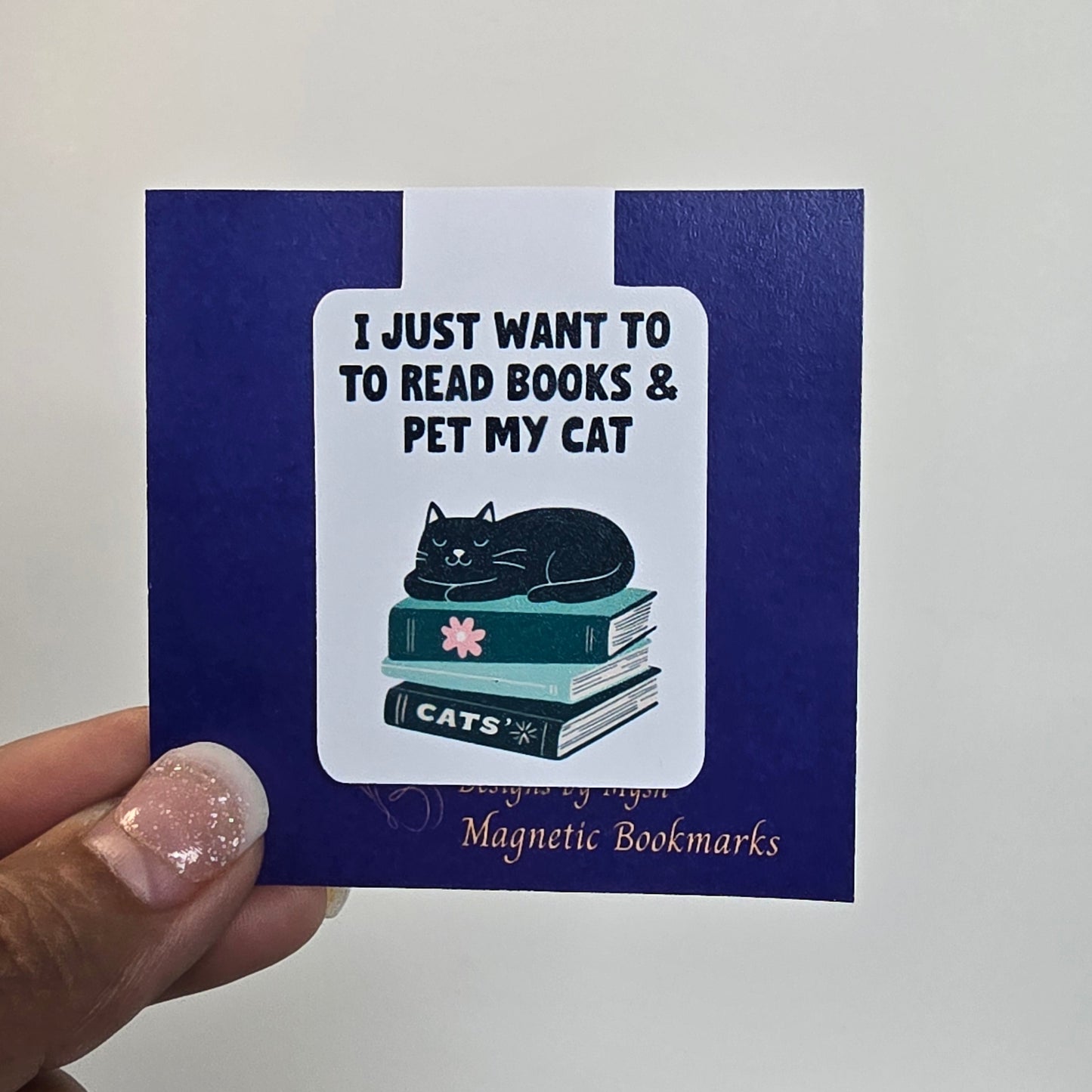 Bookmarks with a cat illustration and text held by a hand against a white background