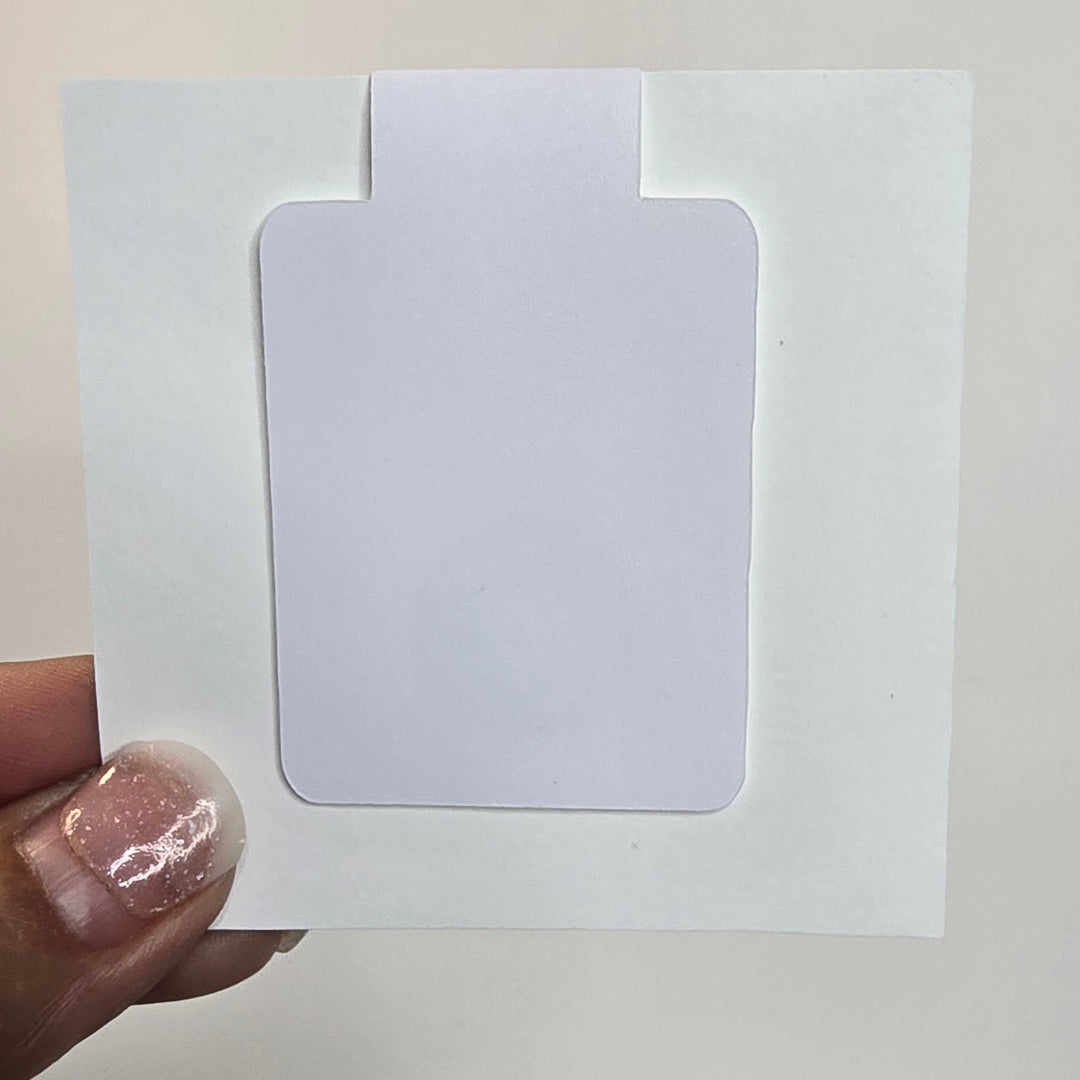 Hand holding a white card with a smaller rectangular cutout against a grid-patterned wall.