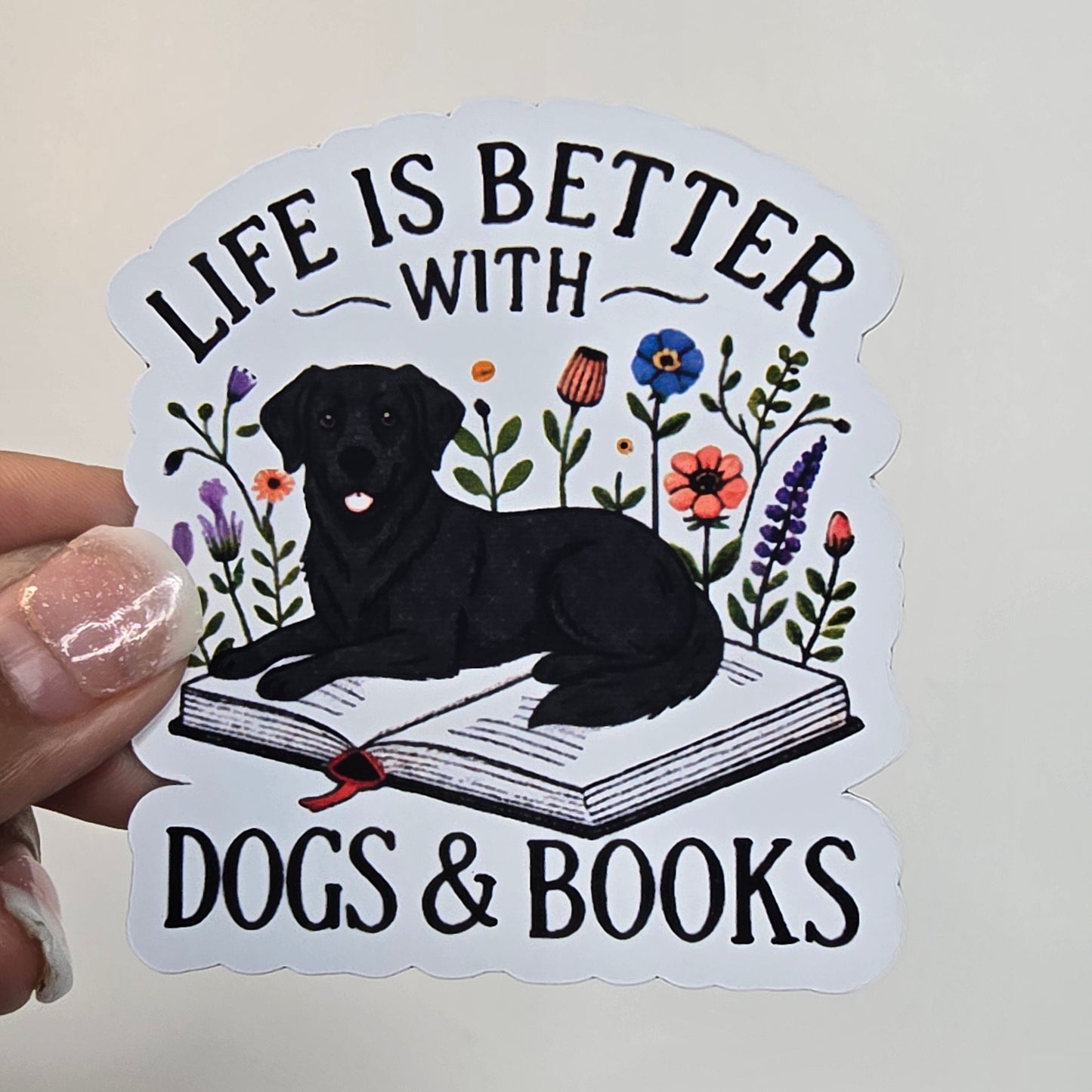 Sticker with a dog, book, and floral design held by a hand against a grid background