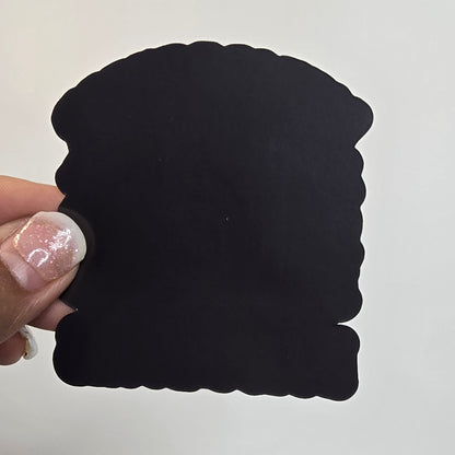 Black square object held by a hand with light nail polish against a white background.