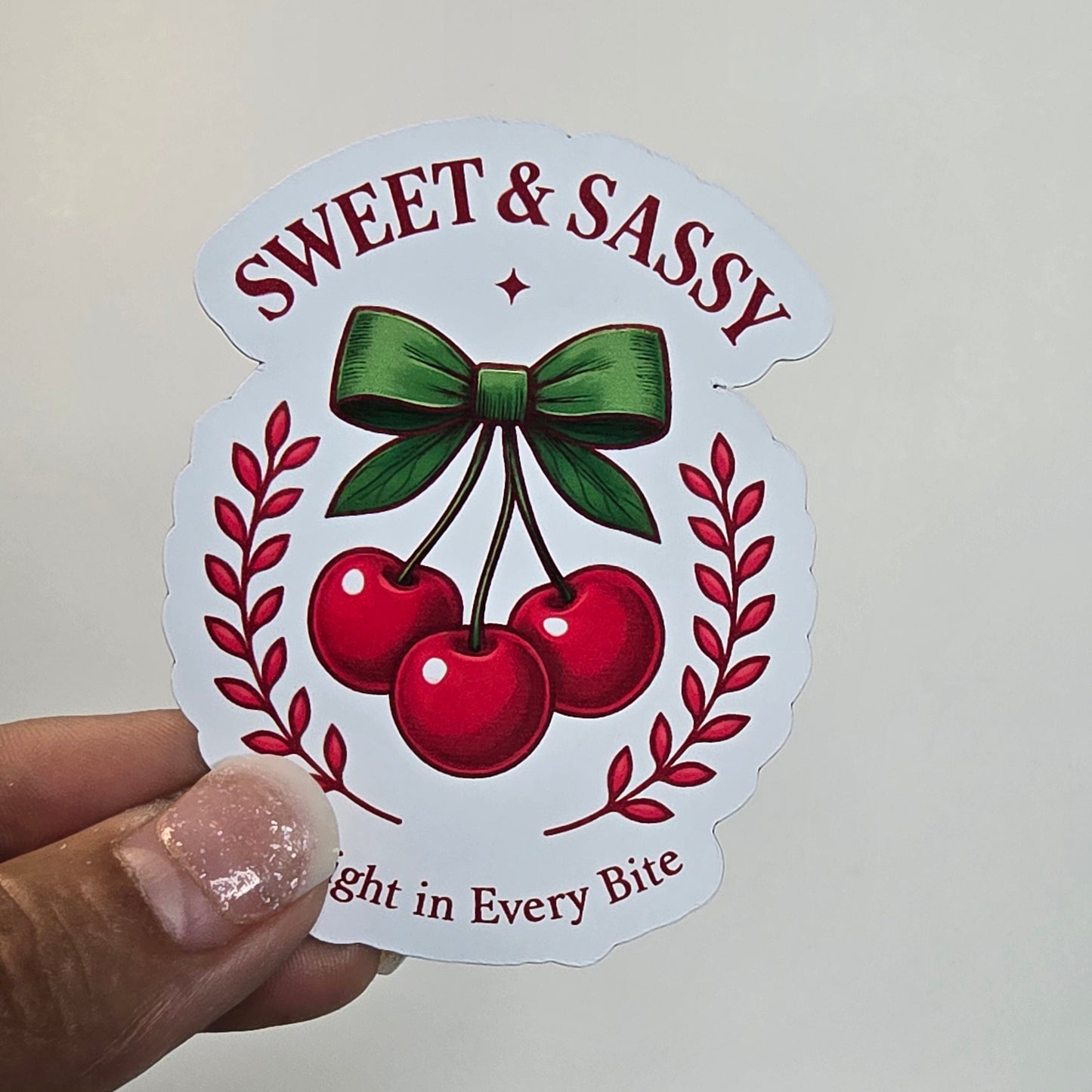 Sticker with cherries and text held by a hand against a grid background