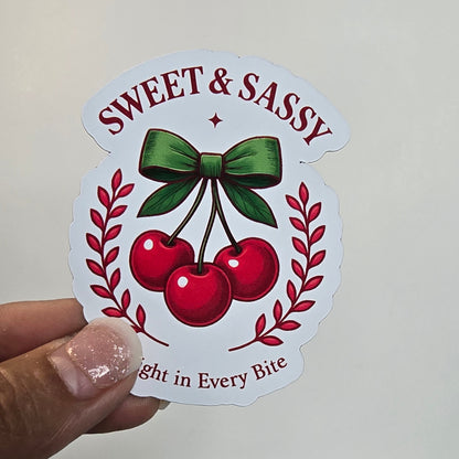 Sticker with cherries and text held by a hand against a grid background