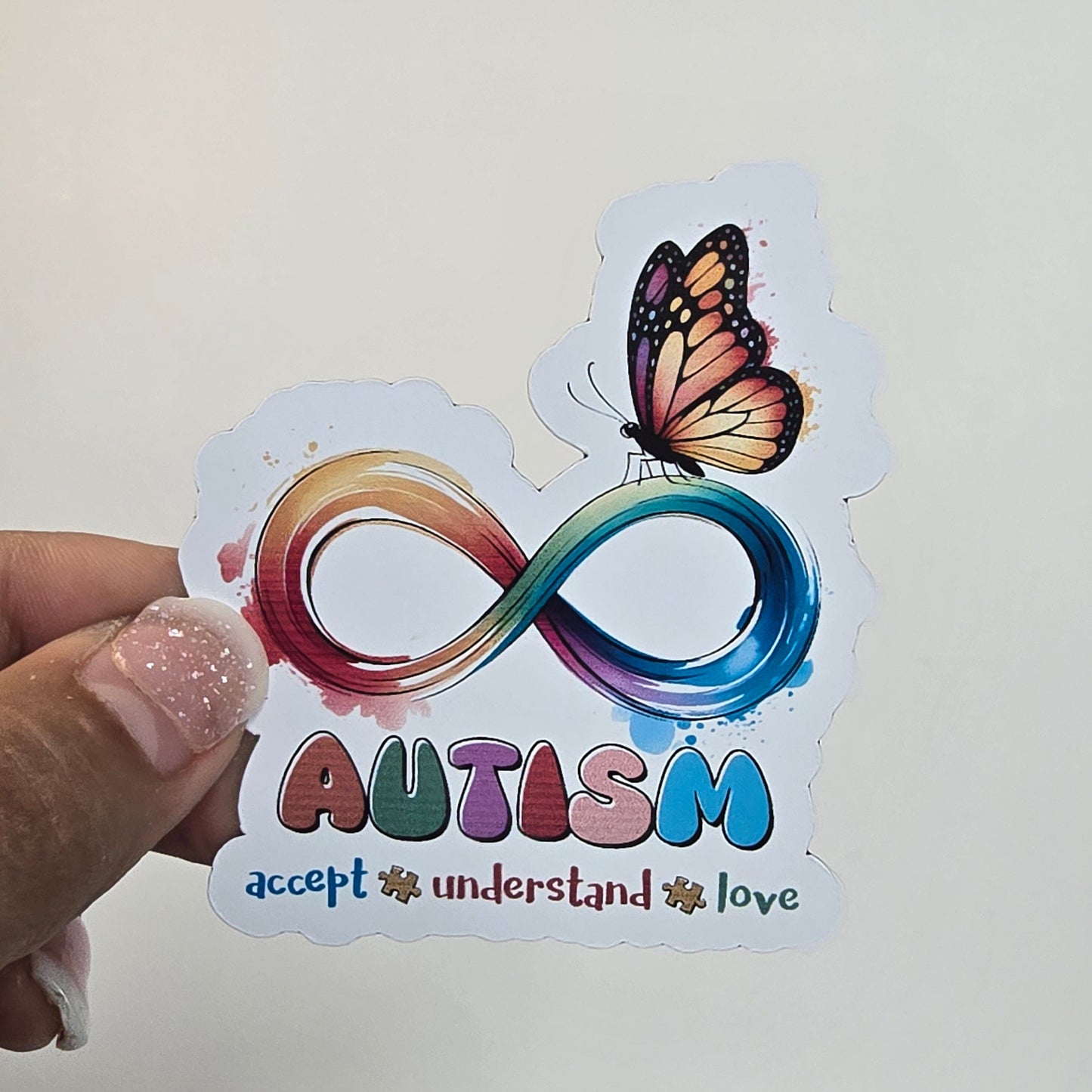 Sticker with autism awareness symbol and butterfly held by a hand against a white background.