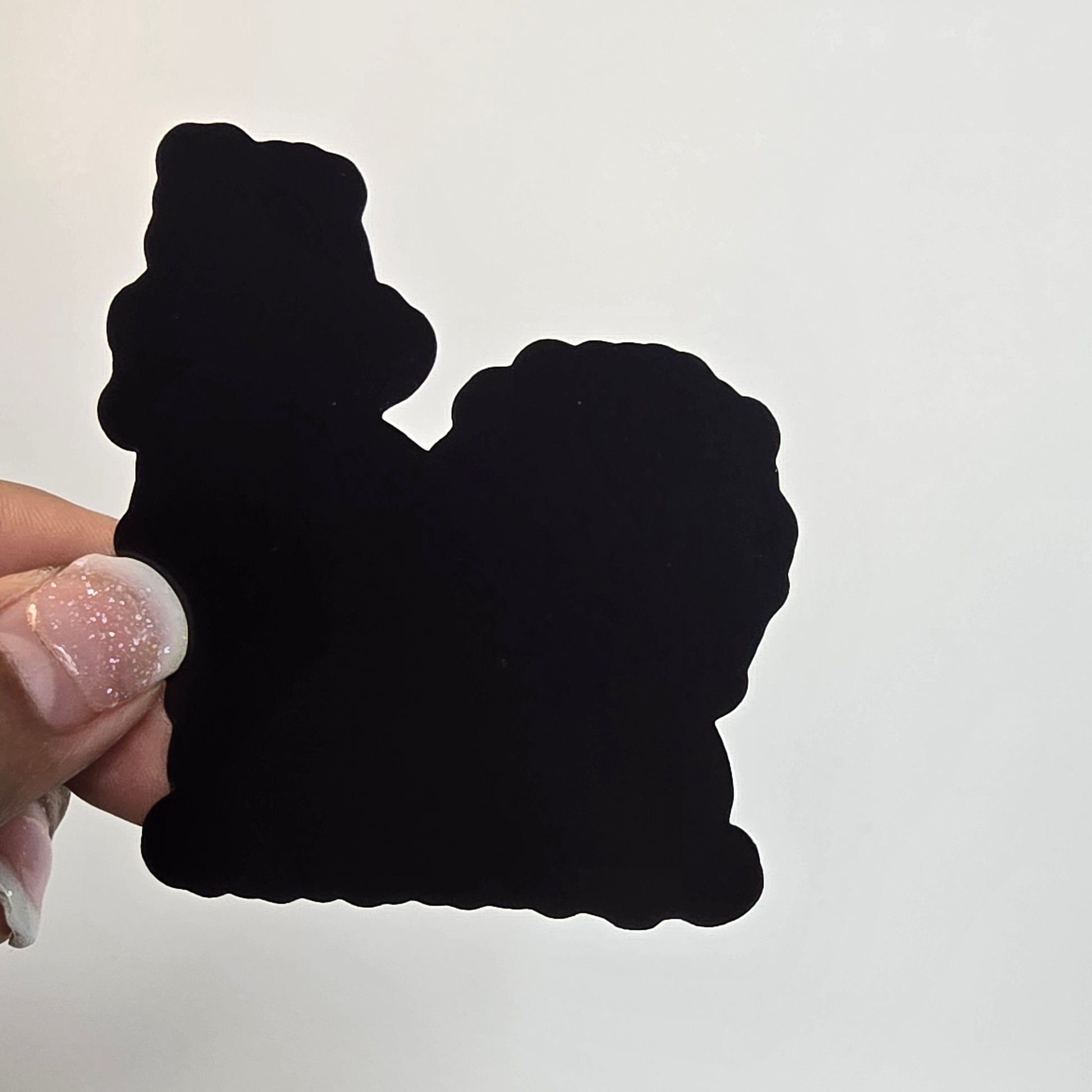 Black cloud-shaped object held by a hand with glittery nail polish against a light background.